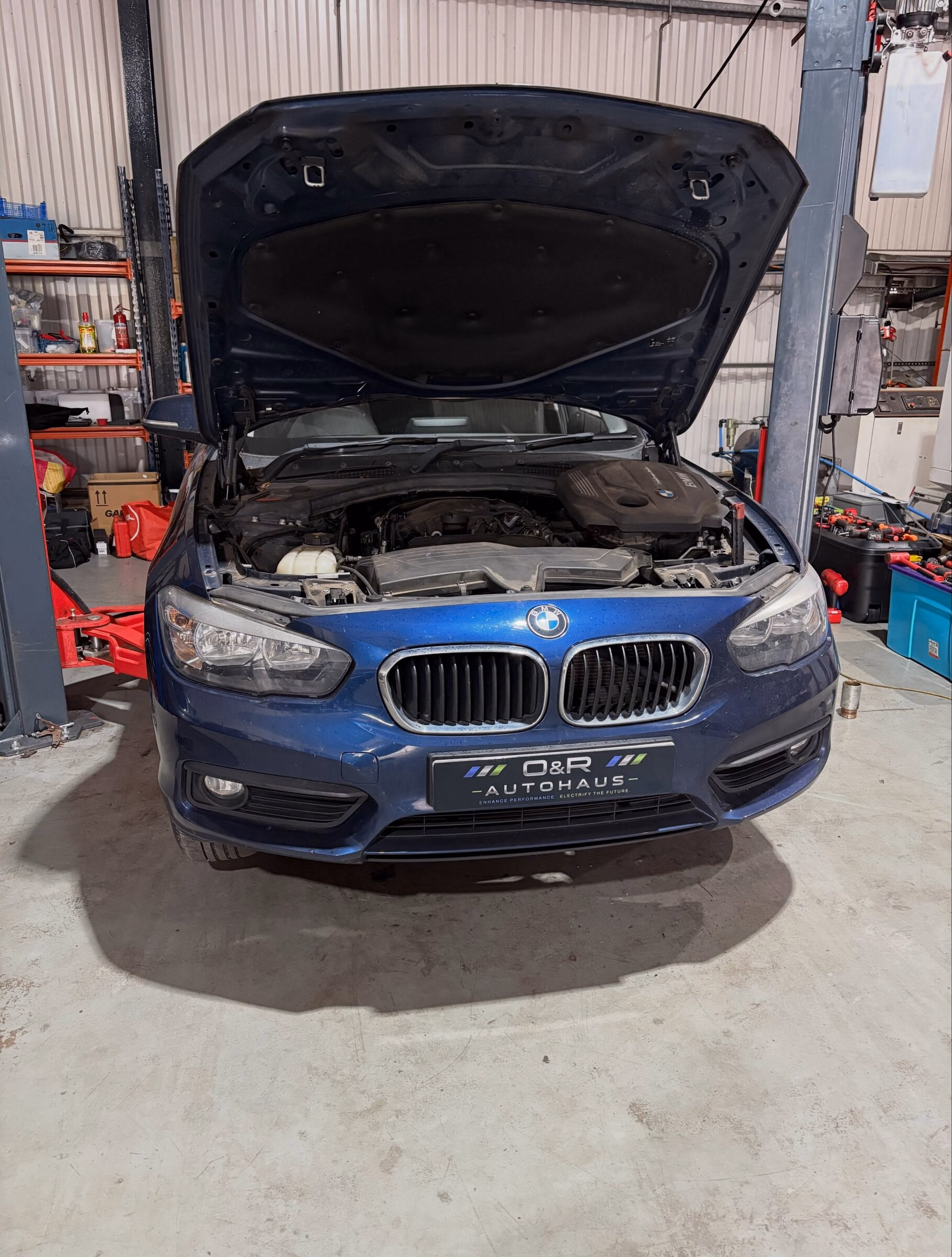 A BMW 1 Series with its bonnet raised between the ramp posts at O&R Autohaus